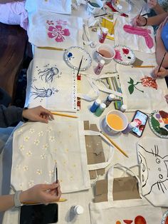 several people sitting at a table with art supplies on it and one person holding a paintbrush