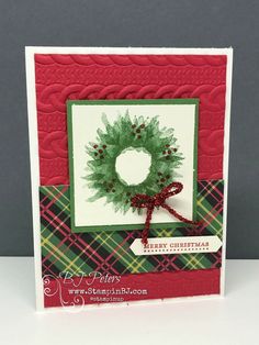 a christmas card with a green wreath and red ribbon on the front, sitting on a table