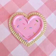 a cookie shaped like a heart with sprinkles on pink and white checkered table cloth