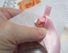 a hand holding a piece of paper with a pink ribbon on it and an orange rose in the background