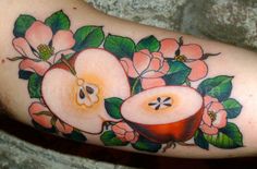 an apple tattoo on the arm with flowers and leaves around it's center piece