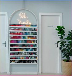 a wall mounted nail polish rack in front of a door with a neon sign above it