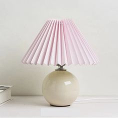 a white table lamp with pink pleated shades on it next to a stack of books