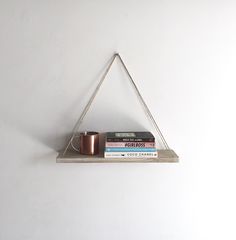 a shelf with books and a cup on it in the shape of a triangle, against a white wall