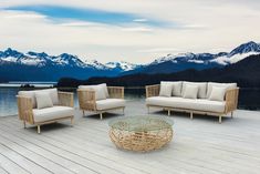 four wicker couches and two chairs on a deck with mountains in the background