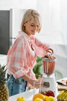 a woman standing in front of a blender filled with fruit