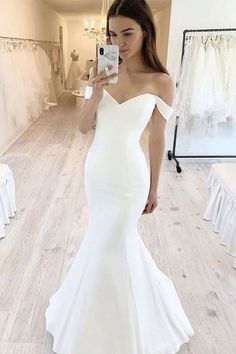 a woman taking a selfie in her wedding dress while wearing a white off the shoulder gown