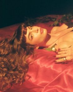 a beautiful woman laying on top of a bed next to a red sheet with flowers