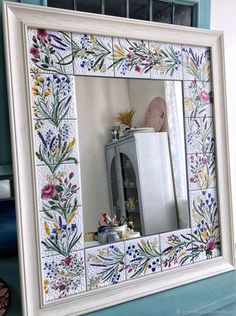 a mirror that is sitting on top of a shelf in front of a wall with flowers and plants painted on it