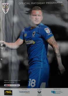 a man with tattoos standing in front of a poster for the soccer team's official matchday program