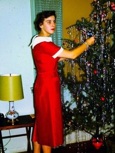 a woman in a red dress standing next to a christmas tree