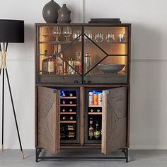 an open cabinet with wine glasses and liquor bottles in it next to a floor lamp