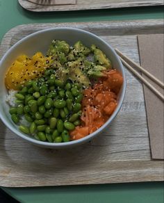 a bowl filled with vegetables and rice on top of a wooden tray next to chopsticks