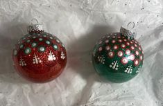 two red and green christmas ornaments sitting on top of a white tablecloth covered surface