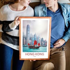 a man and woman holding up a poster with a boat in the water behind them