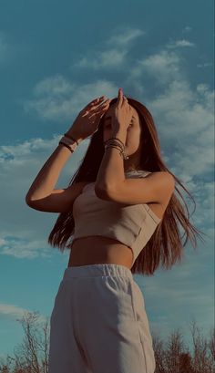 a woman standing in front of a blue sky with her hands on her head and looking into the distance