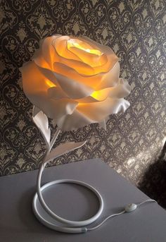 a white rose lamp sitting on top of a table next to a wallpapered wall