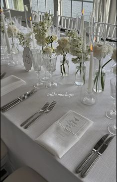 the table is set with silverware and white flowers in vases on top of it