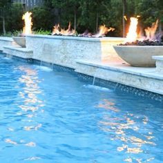 a fire pit in the middle of a pool with blue water and trees behind it