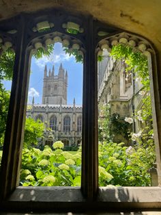 the view from inside an old building looking out onto a garden with flowers and trees