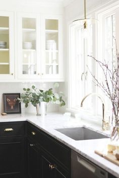 a kitchen with black cabinets and white counter tops, plants in a vase next to the sink