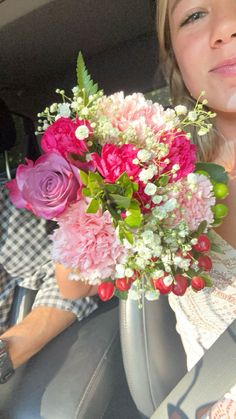 a woman sitting in a car holding a bouquet of pink and white flowers with greenery