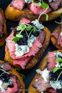 several pieces of bread with meat and blue cheese on top, sitting on a black surface