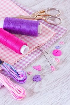 two spools of thread, scissors and buttons on a checkered tablecloth