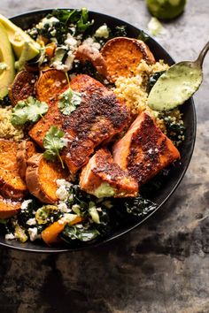 a black bowl filled with meat, vegetables and avocado on top of a table