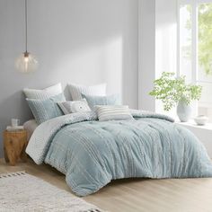 a bedroom with white walls and light blue comforter on the bed, next to a window