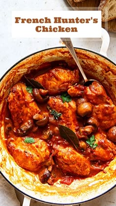 a pan filled with chicken covered in sauce and garnished with parsley next to bread