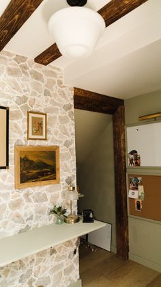 a room with a stone wall and wooden beams on the ceiling is decorated with pictures