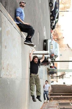 two men hanging off the side of a building while one man is climbing up and down