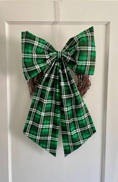 a green and white plaid bow hanging on the front door with fringes attached to it