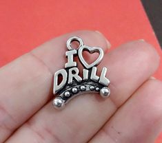 a hand holding a silver charm with the word i love drill in it's center