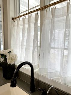 a sink and window with white curtains in the bathroom area, along with a black faucet