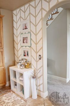 a white shelf with pictures on it in front of a wallpapered entryway