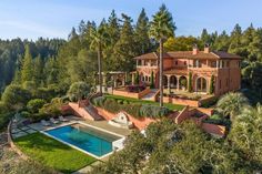 an aerial view of a large house with a pool in the foreground and trees surrounding it