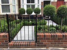 an iron gate in the middle of a brick wall with bushes and shrubs behind it