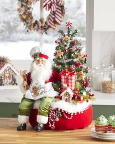 a santa clause figurine sitting next to a christmas tree and cupcakes