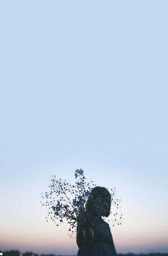 a person holding a bunch of flowers in front of the sky at sunset or dawn