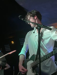 a man holding a guitar in front of a microphone and another person singing into a mic