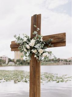 a cross decorated with flowers and greenery in front of the water's edge