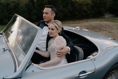 a man and woman sitting in the back of a blue sports car with their arms around each other