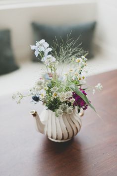 a white vase filled with lots of flowers on top of a wooden table next to a pillow