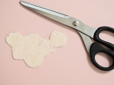 a pair of scissors next to a cut out piece of paper on a pink surface