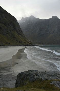 a man sitting in the middle of a river next to some rocks and a mountain