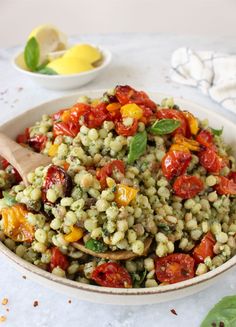 a white bowl filled with green and red food next to a wooden spoon on top of a table