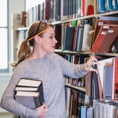 a woman standing in front of a bookshelf holding a book and pointing at it