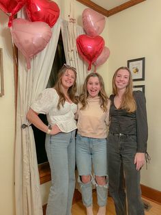 three girls are posing for the camera in front of some heart shaped helium balloons and curtains